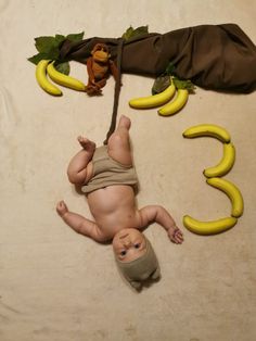 a baby laying on its back next to some bananas and a monkey toy hanging from it's side