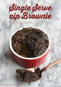 a red bowl filled with brownie next to a spoon on top of a marble counter