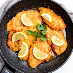 fried chicken with lemons and parsley in a skillet on a white surface