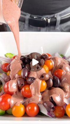 a white bowl filled with lots of different types of vegetables and sauce being poured over it