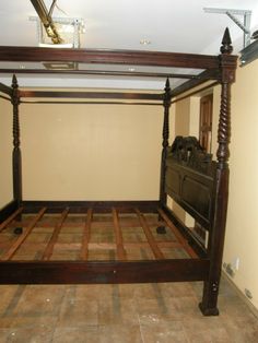 a four poster bed with wooden posts and headboard is in the middle of an empty room