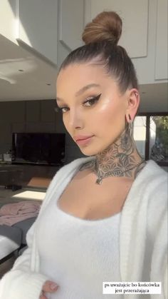 a woman with tattoos on her neck is looking at the camera while wearing a white sweater