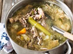 a pot filled with soup and vegetables on top of a wooden table next to a napkin