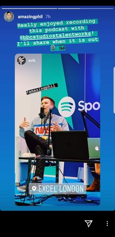 a man sitting in front of a laptop computer on top of a blue table next to a microphone