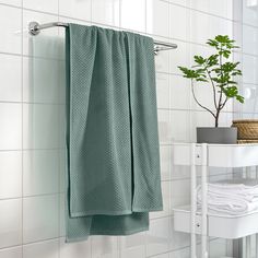 a green towel hanging on the side of a wall next to a white table with a potted plant