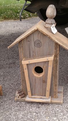 a wooden birdhouse sitting on the ground next to a car