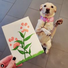 a dog is standing on its hind legs while holding up a piece of paper with flowers painted on it