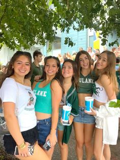 a group of young women standing next to each other in front of a tree holding cups