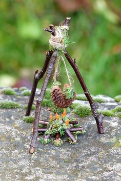 a small sculpture made out of sticks and moss on top of a stone surface with grass growing from it