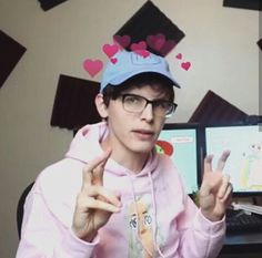 a man wearing a pink hoodie with hearts on his head and holding up two fingers