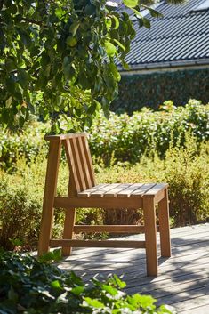 a wooden chair sitting on top of a wooden floor next to a tree and bushes