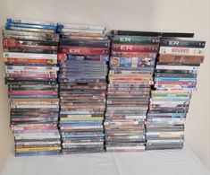 a large stack of dvds sitting on top of a white cloth covered tablecloth in front of a wall