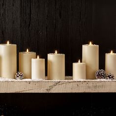 seven lit candles with pine cones and snow on them