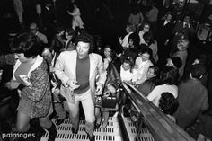 black and white photograph of people on escalators in a crowded building, with one man walking up the stairs