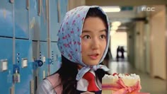 a woman holding a piece of cake next to lockers