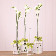 three clear vases with flowers in them on a wooden table next to each other