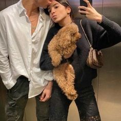 a man and woman standing next to each other in front of an elevator holding a teddy bear