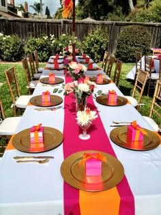 a long table set up with place settings and pink, orange and yellow napkins