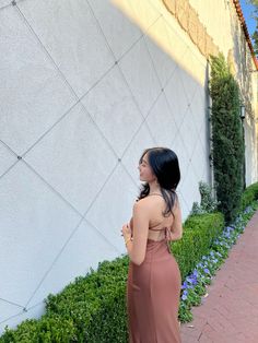 a woman standing in front of a white wall wearing a brown dress and looking back