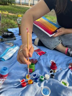 a woman sitting on the ground holding a paintbrush and painting with other paints in front of her