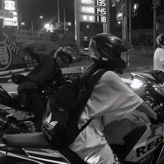 two people riding motorcycles on a city street at night with neon signs in the background