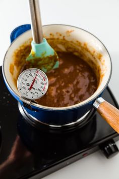 a measuring cup filled with brown liquid on top of a burner next to a thermometer