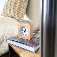 a small wooden clock sitting on top of a table next to a book and lamp