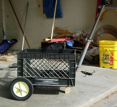 a black cart sitting on top of a cement floor next to a yellow barrel and some tools