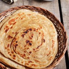 three tortillas in a basket on a wooden table next to some plates and utensils