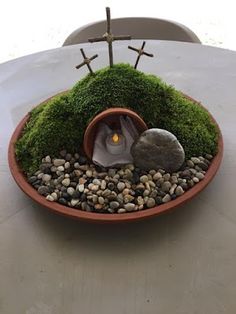 a potted plant with moss and rocks in it sitting on a table next to a cross