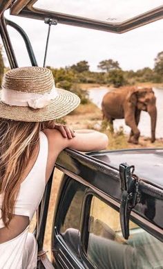 a woman wearing a straw hat looking out the window of a vehicle at an elephant