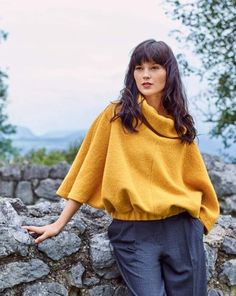 a woman leaning against a rock wall wearing a yellow sweater