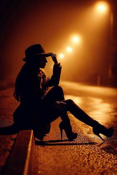 a woman is sitting on the street at night with her legs crossed and holding an umbrella