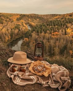 a blanket, hat, and lantern are on the ground in front of a river