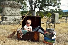 a baby sitting in an old suitcase with books on the ground