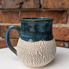 a blue and white mug sitting on top of a table next to a brick wall