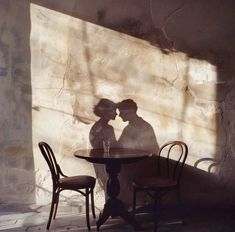 two people sitting at a table in front of a stone wall with the shadow of a kissing couple on it