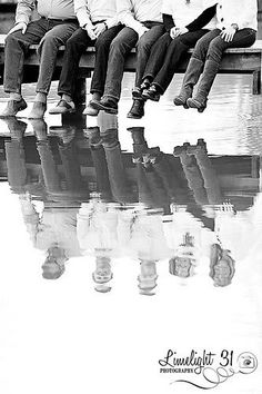 black and white photograph of four people sitting on a bench with their reflection in the water