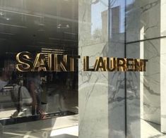 the reflection of people walking in and out of saint laurent's storefront window