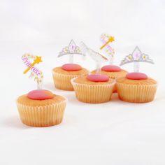 four cupcakes with pink frosting and decorations on top, sitting next to each other