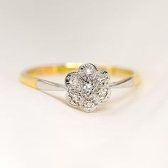 a yellow and white gold ring with a flower design on the side, sitting on a plain surface