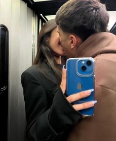 a man and woman kissing while riding on an subway train with their cell phone up to their face