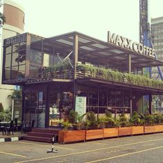 an outdoor cafe with plants growing on the roof and in front of it, next to tall buildings