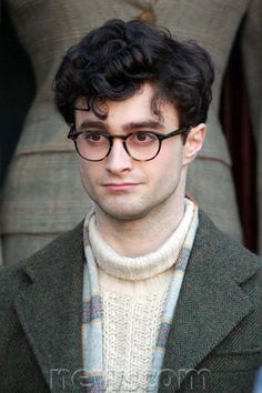 a man wearing glasses and a sweater looks at the camera