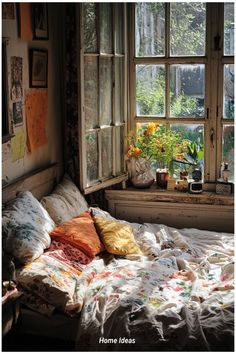 an unmade bed sitting in front of a window with flowers on the windowsill