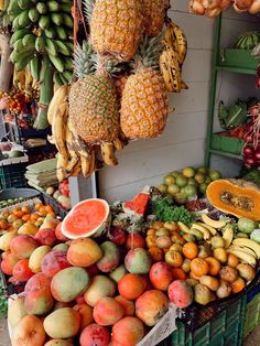 various fruits and vegetables are on display at a fruit stand, including bananas, pineapples, oranges, watermelon, melons