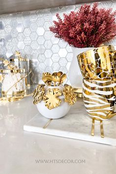 gold and white vases with flowers in them sitting on a marble countertop next to other decorative items