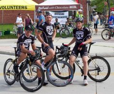 three men are riding their bikes on the street while people walk by in the background