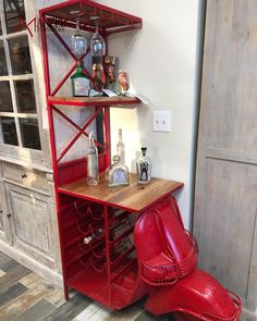 a red chair sitting next to a wooden shelf filled with bottles and glasses on top of it