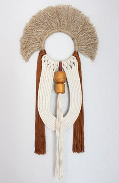 a white wall hanging with two tassels and a wooden bead ball on it